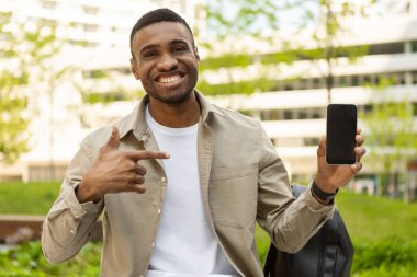 Afro-Amerikalı mutlu bir adam açık hava reklamı için cep telefonunu siyah bir ekranla işaret ediyor. Yüksek kalite fotoğraf