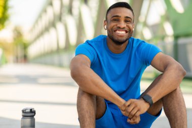 Gülümseyen siyah adam antrenman sırasında yerde oturuyor ve mola veriyor. Yüksek kalite fotoğraf