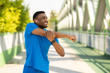 Mavi eşofmanlı atletik Afrikalı Amerikalı bir adam kolunu uzatıyor ve antrenmandan sonra müzik dinliyor. Yüksek kalite fotoğraf