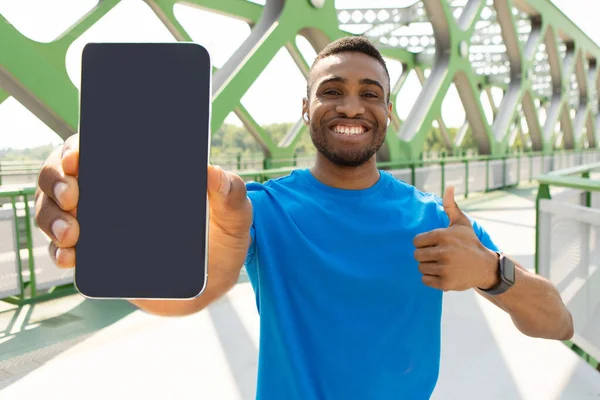 健身应用 肌肉发达的男子拿着装有空白黑屏的智能手机 在镜头前竖起大拇指 高质量的照片 — 图库照片