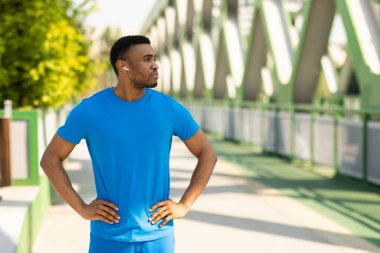 Kablosuz kulaklık takan Afro-Amerikan bir adam park yerinde dikiliyor ve gözünü kaçırıyor. Yüksek kalite fotoğraf