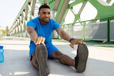 Atletik siyah adam yerde ısınırken müzik dinlemek için akıllı telefon teknolojisi kullanıyor. Yüksek kalite fotoğraf