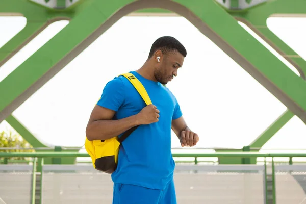 Side view of African American man checking health data on smartwatch after jogging in the park. High quality photo