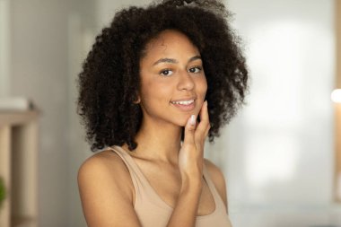 Gülümseyen Afrikalı Amerikalı kadın kameraya bakarken yüz nemlendirici sürüyor. Yüksek kalite fotoğraf