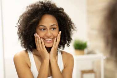 Aynanın yanındaki banyoda yüz bakımı yaptıktan sonra gülümseyen güzel bir kadın. Yüksek kalite fotoğraf