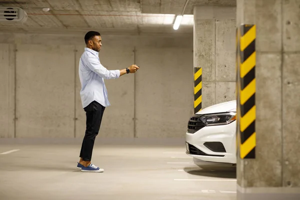 African american man with car keys in front of car in underground parking. High quality photo