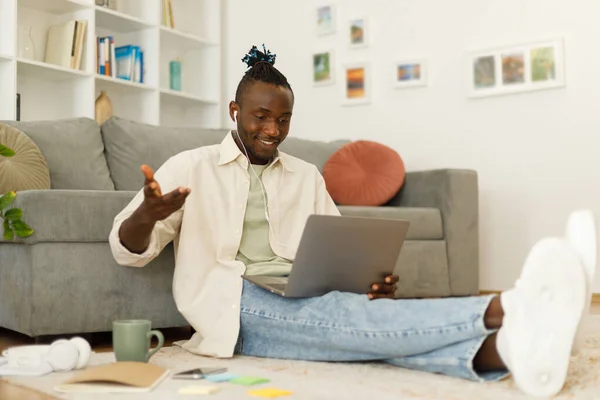 Happy man relaxing near sofa during video call using laptop at home. African american man sitting near sofa and making video call. High quality photo