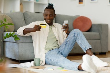 African young man shopping online with credit card using smartphone at home. In room. High quality photo