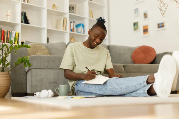African American teenage student taking notes for an exam while distance learning at home. Black guy working on his homework writing paper. High quality photo