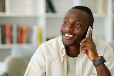 Portrait of a young smiling black man using a mobile phone, talking on it, smiling towards the window. High quality photo