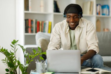 Young black freelancer guy working on laptop while sitting at table in living room at home office, free copy space. High quality photo