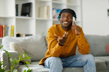 Phone call. Happy afro man talking on mobile phone while sitting on sofa at home. High quality photo