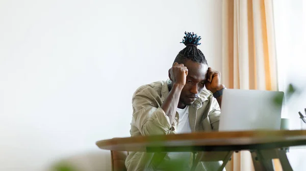 A man sits at home in a tense mood and looks at a laptop. The man looks flustered, with hands touching his head. High quality photo