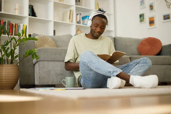 Smart black teenage student in full growth with a book makes notes. Smart teenager writing assignment or term paper, studying remotely indoors. High quality photo