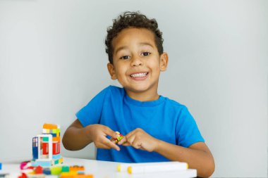 A small child plays with many colorful plastic toys indoors. Little boy playing at home with Lego building blocks. Child and toys. High quality photo