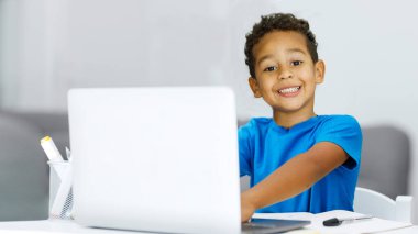 Little black boy rejoices at studying with a laptop at home, recommends online education, copy space. High quality photo