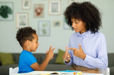 A smart boy counts on his fingers, studies with a private teacher in the office, a child learns numbers and how to count, sits at a table with a tutor. High quality photo
