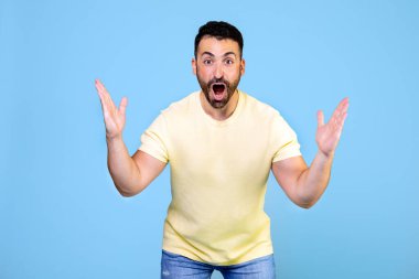 Angry and furious man on a blue background. He throws up his hands in rage and screams. High quality photo