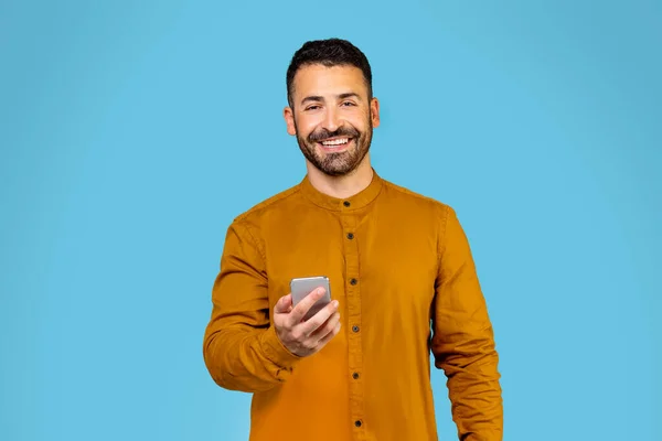 A european man using a mobile application on his phone or sending text messages while standing in a studio on a blue background. High quality photo