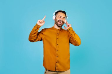 Cheerful middle eastern man listening to music with wireless headphones and singing. High quality photo