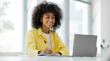 Happy black brunette woman using laptop smiling while working while sitting at workplace in modern office. High quality photo