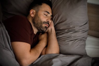 Sakallı sakin genç bir adam yatak odasının içindeki battaniyenin altında yumuşak bir yastığın üzerinde uyuyor. Yüksek kalite fotoğraf