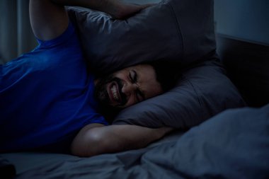 Genç bir Arap adam, evinde gürültüden iki eliyle kulaklarını kapatan bir yastık tutuyor, uykusuz bir gece, boş alana yakın çekim. Yüksek kalite fotoğraf