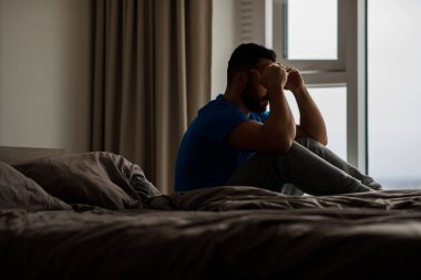 Mutsuz bir adam yatakta oturup sorunları, depresyonu ve elleriyle yüzünü kapatmayı düşünüyor. Yüksek kalite fotoğraf