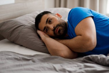 Pijamalı bunalımlı bir adam yatağında yatıyor ve kendini kötü hissediyor. Yüksek kalite fotoğraf