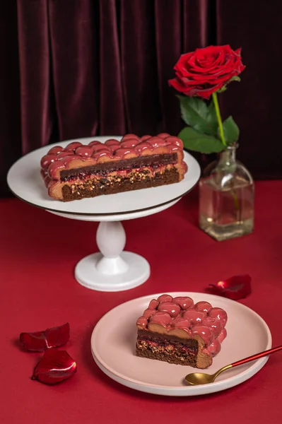 Mousse cake with red mirror icing. Cutaway cake: chocolate sponge cake, crunchy layer, cherry confit, cherry cream, chocolate mousse. Piece of cake.