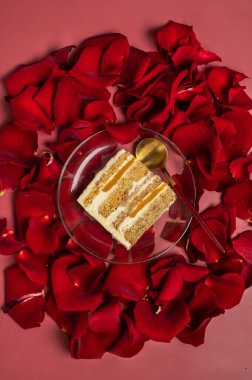 Pembe arka planda kırmızı gül yapraklı bir dilim bisküvi pastası. Yukarıdan bak. Romantik atmosfer, aşıklar için pasta.