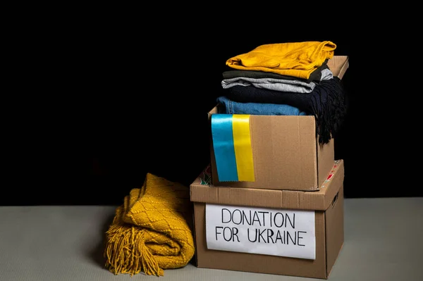 Box with donation clothes for ukrainian refugees suffering from war. Charity and Helping poor and needy people. Stay with Ukraine