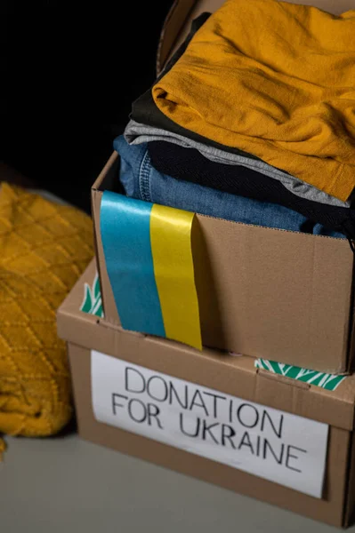 Volunteer packing clothes in donation box with Ukrainian flag. Boxes on a black background.