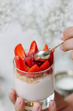Elinde taze çilek ve krem peynirli bir bardakta çilekli cheesecake. Tatmak.