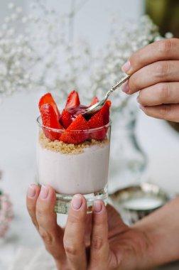 Elinde taze çilek ve krem peynirli bir bardakta çilekli cheesecake. Tatmak.