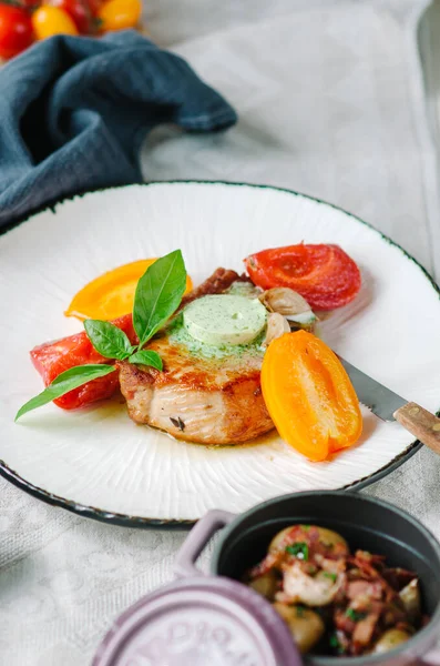 Kemiğin üzerinde yeşil tereyağlı domuz filetosu. Fırında domates, konserve sarımsak ve domuz pastırmalı kızarmış patates..