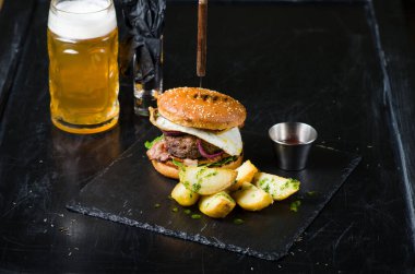 Yağda yumurta, domuz pastırması, soğan, domates ve marullu leziz bir hamburger. Barda biralı bir burger.