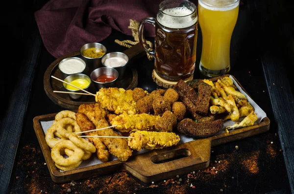 Metal tray with beer snacks, combined beer snacks, croutons and two mugs of beer. Rye breadcrumbs, breaded cheese on a stick, breaded meat, fish in batter and sauces.