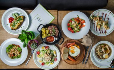 Arkadaşlarla ya da akrabalarla akşam yemeği. Restoran yemeği konsepti. Sezar salatası, İngiliz kahvaltısı, pirzola bifteği, fırında patates, somon krepi, ramen ve sebze salatası..