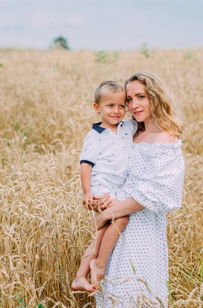 Happy family. A young woman with blond curly hair is holding a wheat field against the background. Mother and son. Summer mood. Ukrainian family.