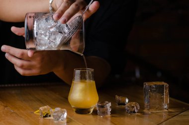 Profesyonel barmen tezgahta buzlu bir kokteyl hazırlar. Kandurin eklenmiş sarı alkollü kokteyl.