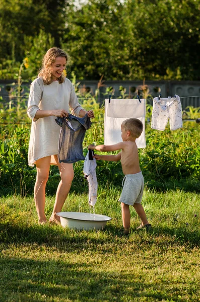 Woman with children in garden hanging laundry outside, lifestyle people concept. The son helps his mother hang up clothes, have fun.