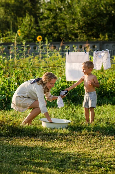 Woman with children in garden hanging laundry outside, lifestyle people concept. The son helps his mother hang up clothes, have fun.