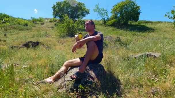 一个男人坐在石头上喝水 — 图库视频影像