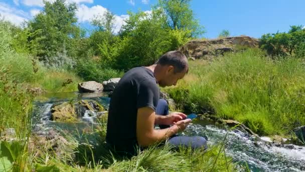 Een Man Die Smartphone Bij Rivier Klikt Speelt — Stockvideo