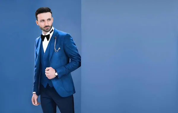 Takım elbiseli yakışıklı iş adamının portresi mavi arka planda fotokopi alanı ile duruyor.