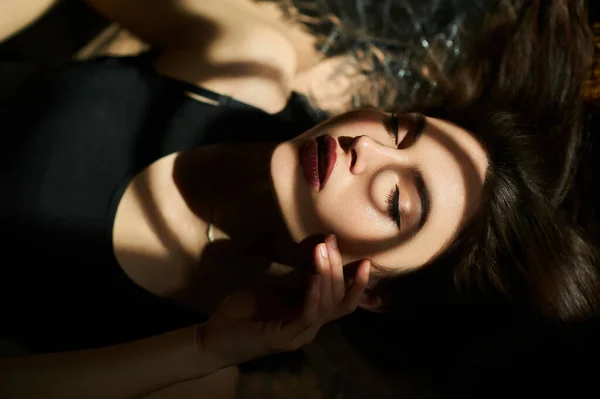 Portrait of a young girl lying with her eyes closed, with a shadow pattern on her face, touching the skin with her beautiful cheek.
