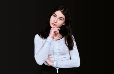 Beyaz bluzlu, büyük göğüslü, başını eliyle dinlendiren esmer kız, hayali bir şekilde başını eğik bir şekilde kameraya bakar, siyah arka planda durur. Pankart, metin için yer.