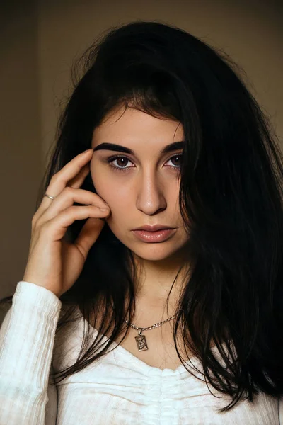 Siyah saçlı, beyaz kazaklı güzel bir kızın moda fotoğrafı, baş tapınağında el ele tutuşuyor. Kadın portresi..