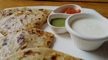 Yoğurt, turşu ve yeşil turşuyla servis edilen popüler Hint yemeği Aloo Paratha 'nın yakın çekim görüntüleri.